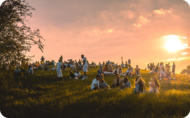 People sitting and socializing on a grassy hill during sunset