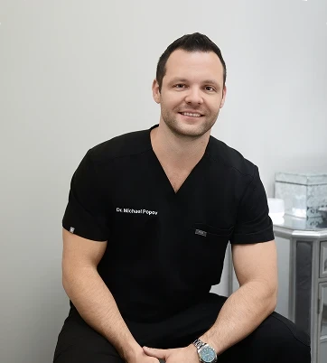 Man in black scrubs sitting on a chair, smiling at the camera. Neutral background